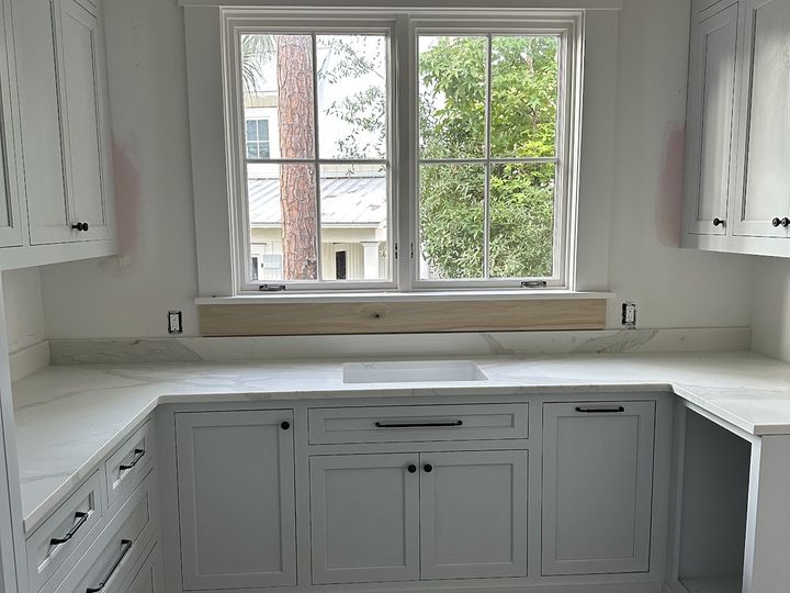 White cabinets and quartz counters around a window sink, by SV Construction
